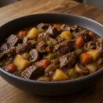 Thick brown ale stew with cubed meat, potatoes, carrots, celery, and mushrooms in a ceramic bowl