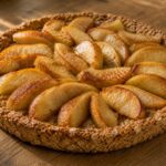 Round golden oat tart topped with glossy roasted apple wedges on a warm wooden table