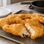 Golden beer batter fried fish draining on a wire rack over a baking sheet