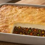 Square casserole of biscuit-topped shepherd’s pie showing golden biscuit crust, creamy potatoes, tomato beef, and mixed vegetables
