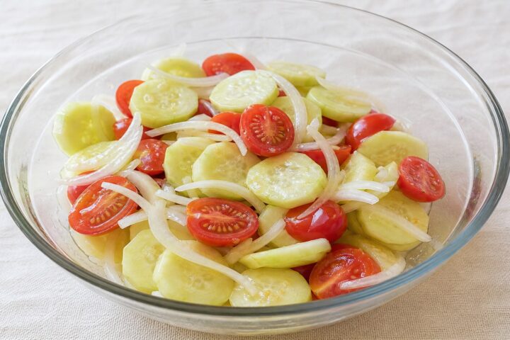 Cucumber tomato and onion salad with peeled cucumber slices, halved cherry tomatoes, and sweet onion in vinaigrette