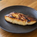 Caramelized black cod fillet with browned miso glaze on a dark ceramic plate
