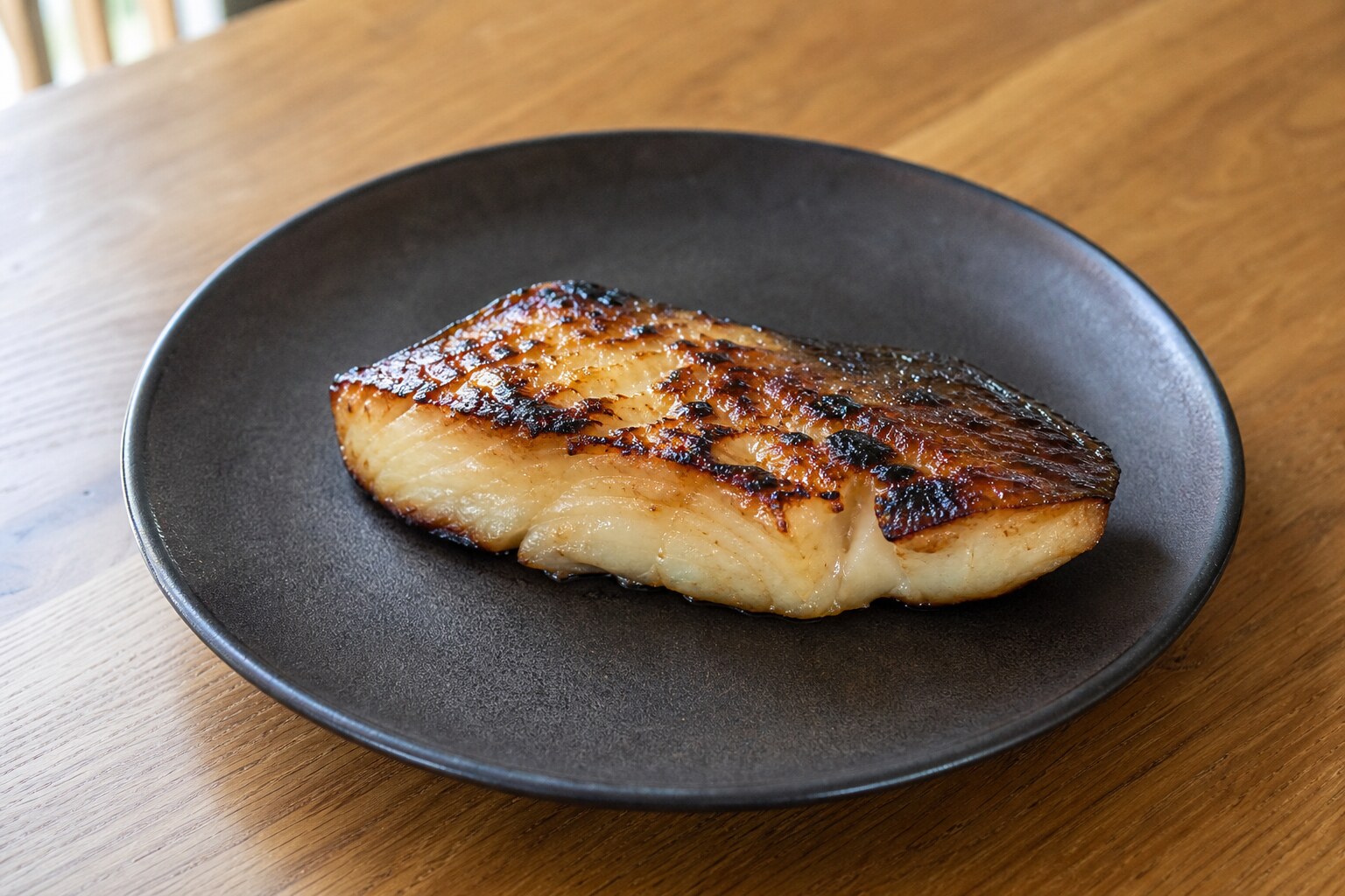 Caramelized black cod fillet with browned miso glaze on a dark ceramic plate