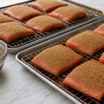 Molasses-brined salmon portions coated with brown sugar and lemon pepper on wire racks over sheet pans