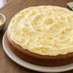 Pale pineapple cream topping spread in soft swirls over a plain round cake with crushed pineapple visible