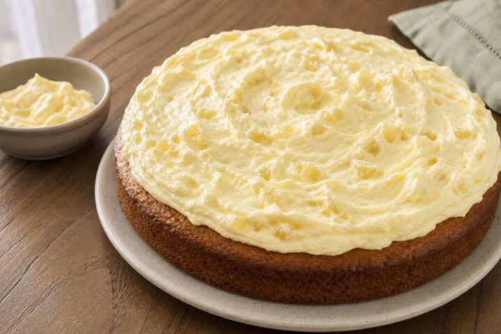 Pale pineapple cream topping spread in soft swirls over a plain round cake with crushed pineapple visible