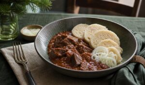 Prague beef goulash with tender beef cubes, red-brown paprika sauce, bread dumplings, and sliced onion