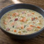 Creamy salmon chowder with red-skinned potato pieces, carrots, celery, and dill in a dark bowl
