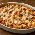 Baked rigatoni in orange tomato cream sauce with browned meat and melted mozzarella in a ceramic dish