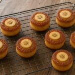Eight golden mini muffins with caramelized banana rounds on a wire cooling rack