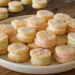Round sugar-coated cream wafer sandwich cookies with pale vanilla and restrained pastel butter fillings on a ceramic platter
