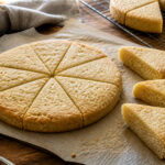 Thick pale-golden shortbread rounds scored into fork-pricked wedges with separated pieces showing a crumbly interior