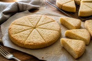 Thick pale-golden shortbread rounds scored into fork-pricked wedges with separated pieces showing a crumbly interior