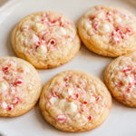 Pale golden cookies with white chocolate chips and crushed red-and-white peppermint candy on a white plate.