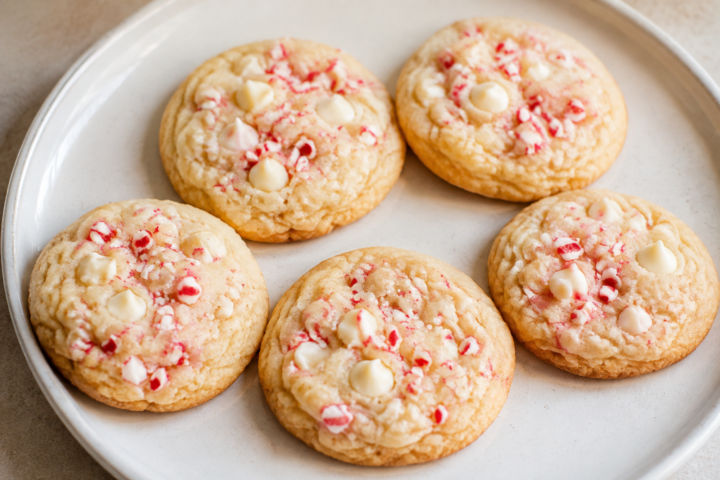 Pale golden cookies with white chocolate chips and crushed red-and-white peppermint candy on a white plate.